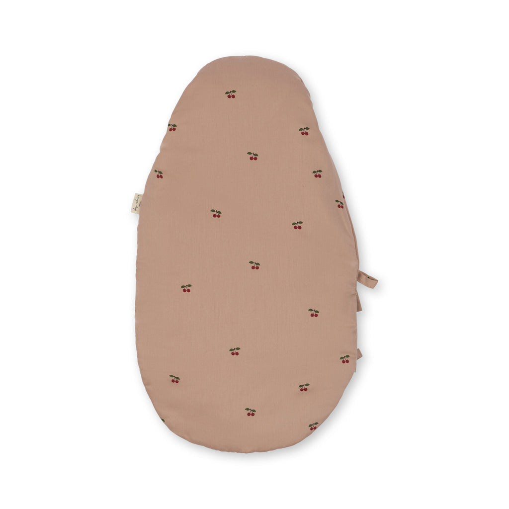 The Konges Sloejd Doll Sleeping Bag in Cherry Blush is a light brown, oval-shaped lounger made from organic cotton with cherry prints. It has subtle side ties, a soft padded texture with recycled polyester filling, and is shown on a white background.