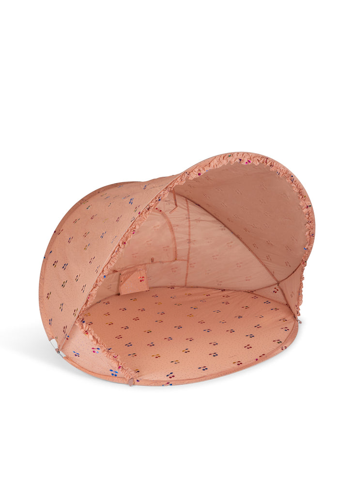 The Konges Sloejd Lace Pop-Up Beach Tent UPF 50+ is a collapsible, peach-colored pet tent with a curved canopy and multicolored paw prints, offering UV protection, shown on a white background.