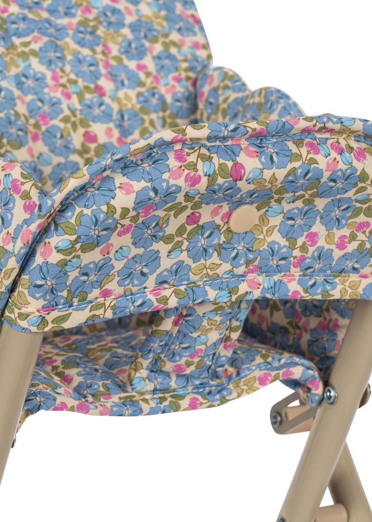 A close-up of the Konges Sloejd High Chair - Rose Flower, a foldable doll high chair with a beige metal frame and a removable fabric seat featuring a blue and pink rose flower pattern with green leaves.