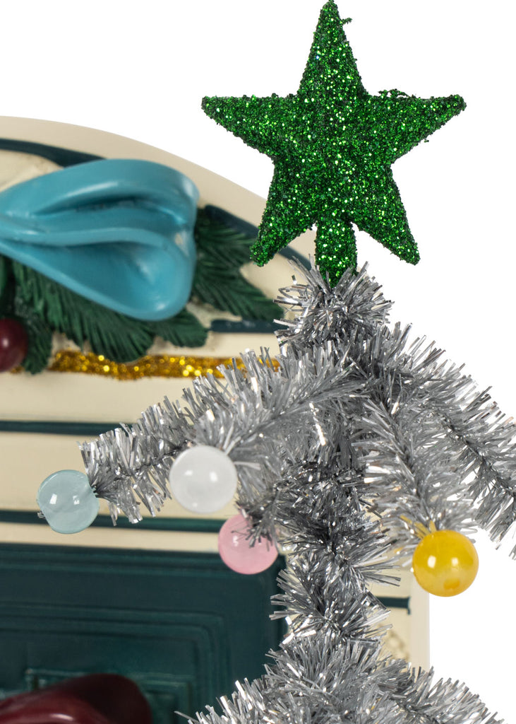 A miniature silver tinsel Christmas tree with a green glittery star and pastel ornaments placed in front of a Konges Sloejd Christmas Door.
