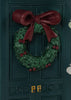 The Konges Sloejd Christmas Door is a miniature dark green elf door featuring a festive holly wreath with a large burgundy bow and two brass-colored door handles.