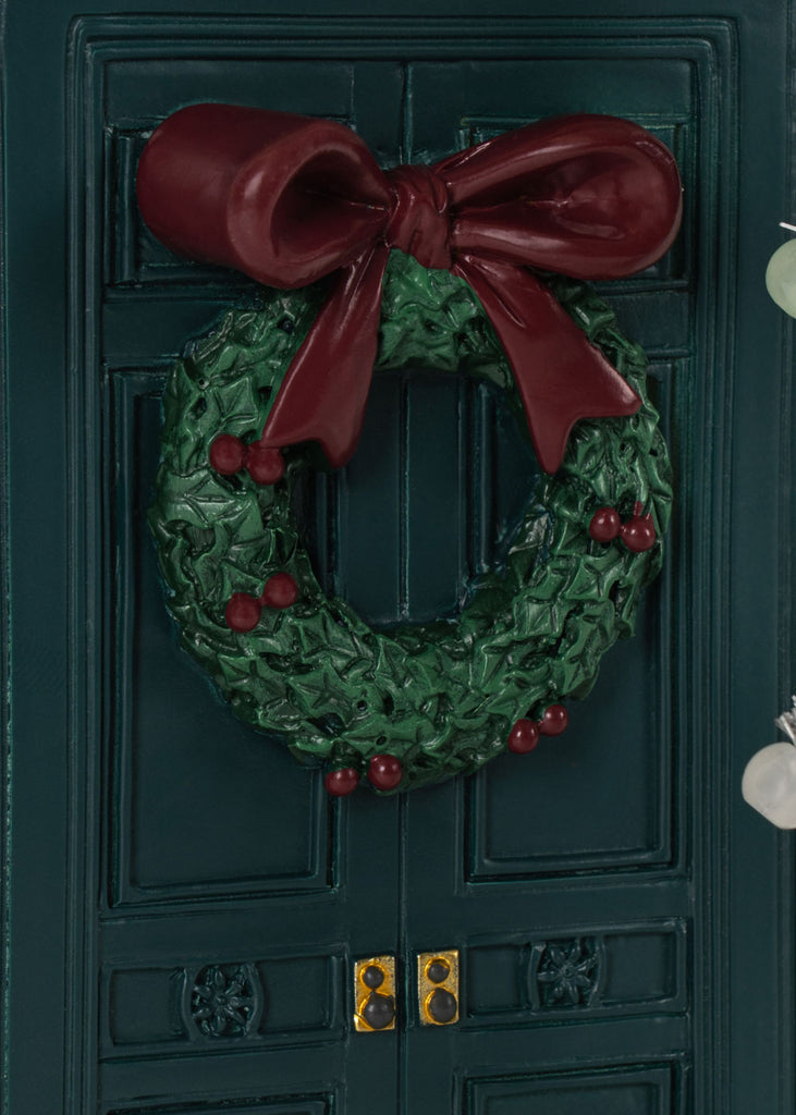 The Konges Sloejd Christmas Door is a miniature dark green elf door featuring a festive holly wreath with a large burgundy bow and two brass-colored door handles.