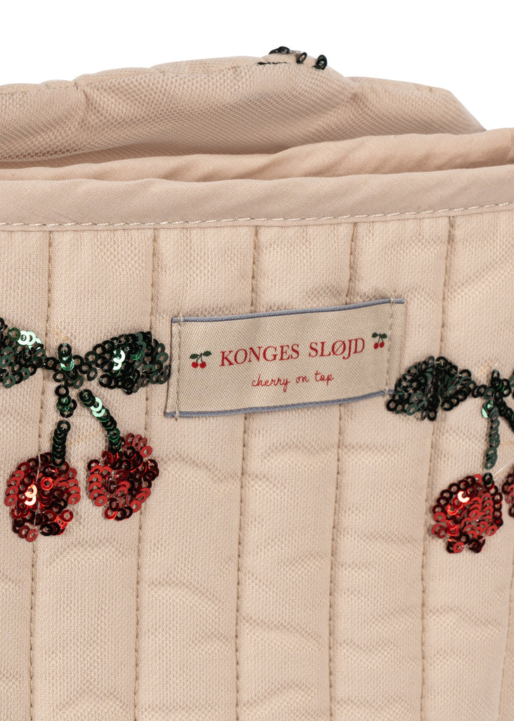 Close-up of the quilted beige fabric and red sequin-embroidered cherries on the Konges Sloejd Tulle Doll Stroller - Cherry Sequin, featuring a removable "KONGES SLOJD cherry on top" label.