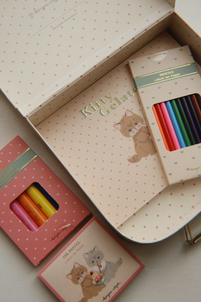 An open Konges Sloejd Little Artist Set - Kitty Friends featuring a sketchbook with a kitty illustration, a set of colored pencils, and a set of oil pastels.