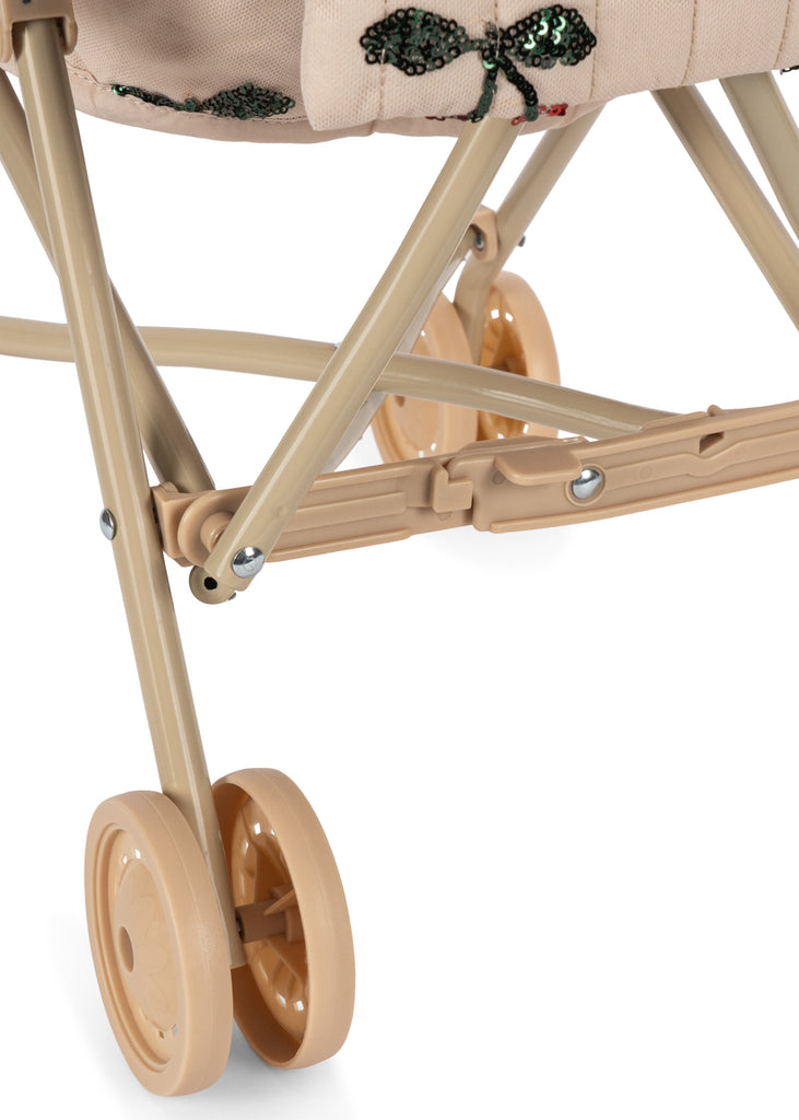 Close-up of the Konges Sloejd Tulle Doll Stroller - Cherry Sequin, showing four small plastic wheels, the metal frame, and fabric with a sequin butterfly design.