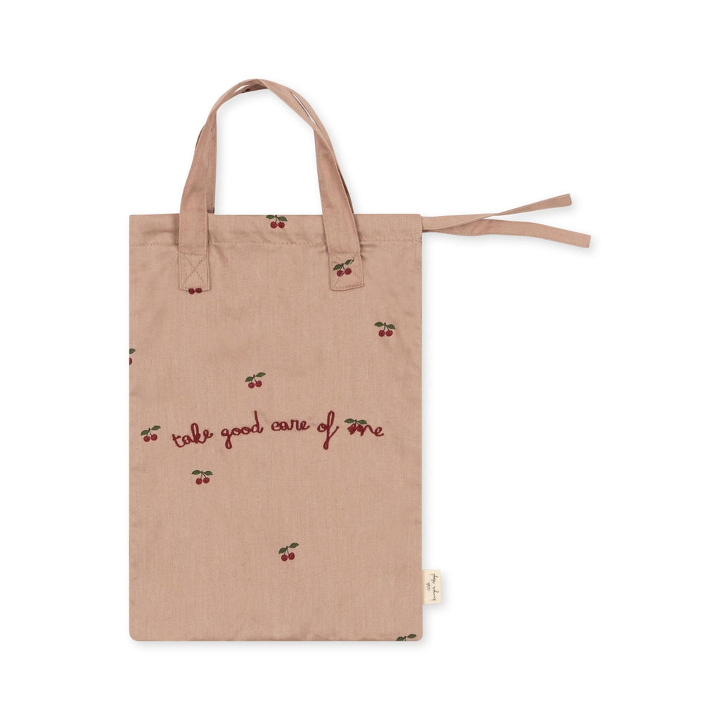 The Konges Sloejd Doll Nursery Set - Cherry Blush is a light brown fabric bag with short handles, a side tie, cherry patterns, and “take good care of me” embroidered in red; ideal for storing doll accessories.