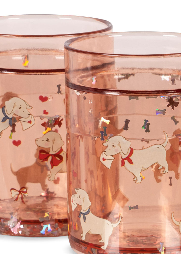 The Konges Sloejd Glitter Cups - Woof Letter Rose (2 Pack) feature pink kids' drinkware with white dogs in red bows holding envelopes, plus hearts and colorful bone confetti—ideal for fun dinnerware collections.