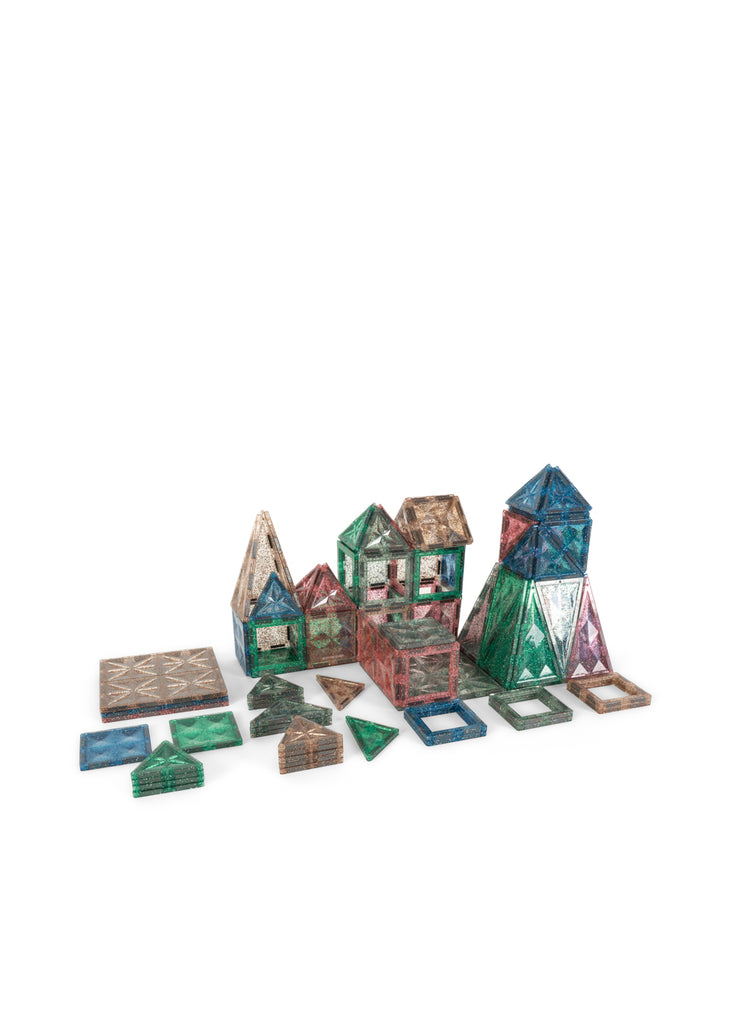 Translucent, glittery magnetic tiles from the Konges Sloejd Piece By Piece Magentic Building Set are assembled into small structures and geometric shapes to encourage fine motor skills.