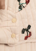 Close-up of the Konges Sloejd Mini Tulle Doll Pram - Cherry Sequin, showing beige quilted fabric with two cream snap buttons and embroidered sequin cherries with green leaves and red fruit.