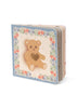 The Konges Sloejd Touch and Feel Book features a sensory cover with a brown teddy bear with a heart on its chest, framed by a floral border on blue. Perfect for little hands, this interactive book invites babies to explore different textures.