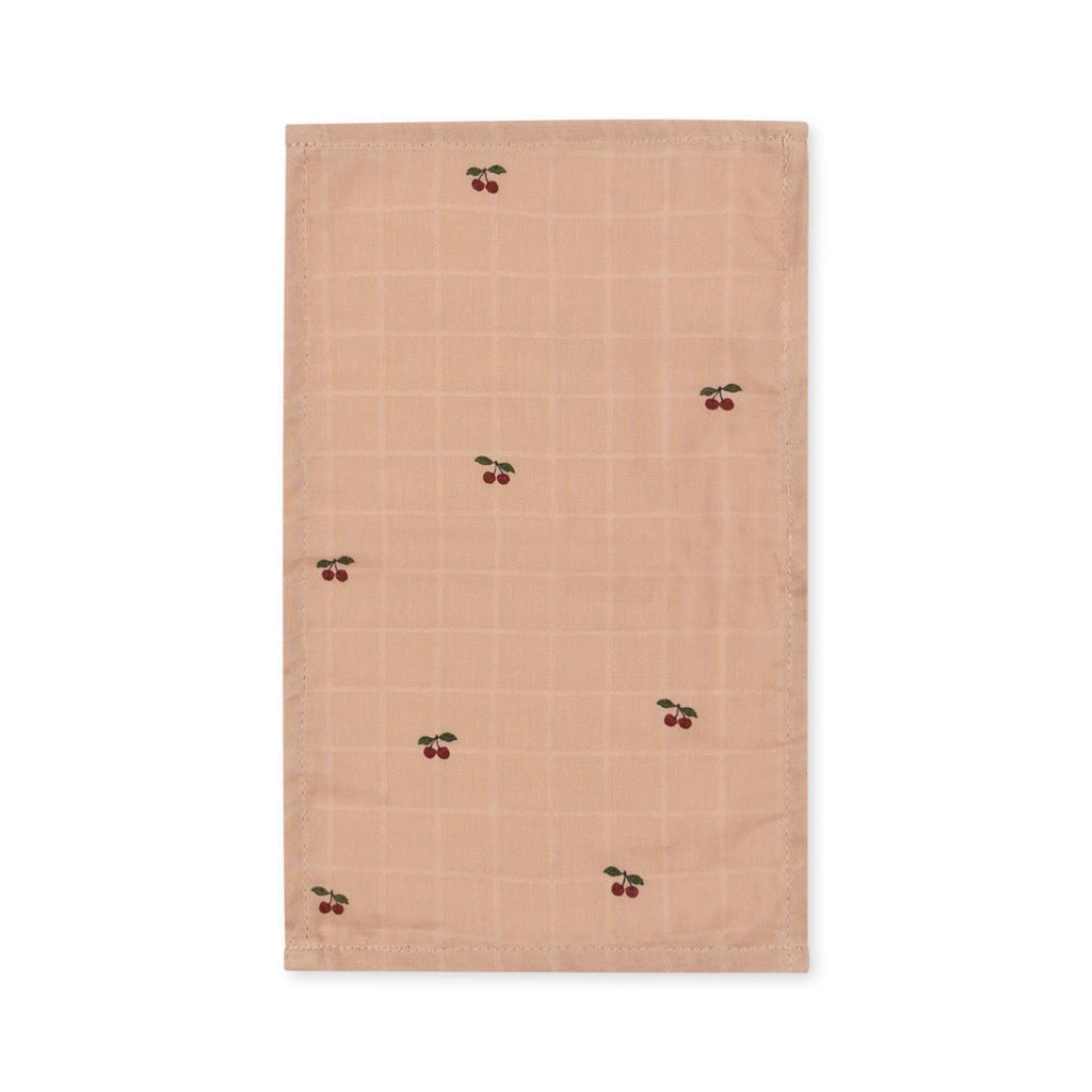The Konges Sloejd Doll Nursery Set - Cherry Blush features a light brown organic cotton cloth napkin with a subtle checkered pattern and embroidered red cherries—ideal to pair with the matching organic cotton doll bib set.