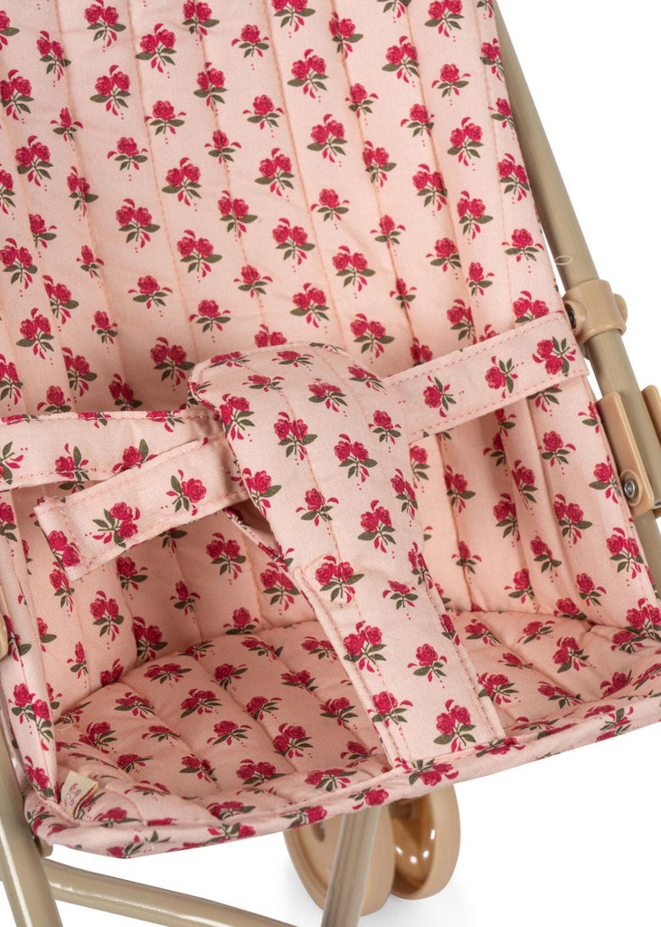 Close-up of the Konges Sloejd Doll Stroller - Rosie Rose, showing pink fabric with red rose and green stem pattern, beige frame, and visible safety straps.
