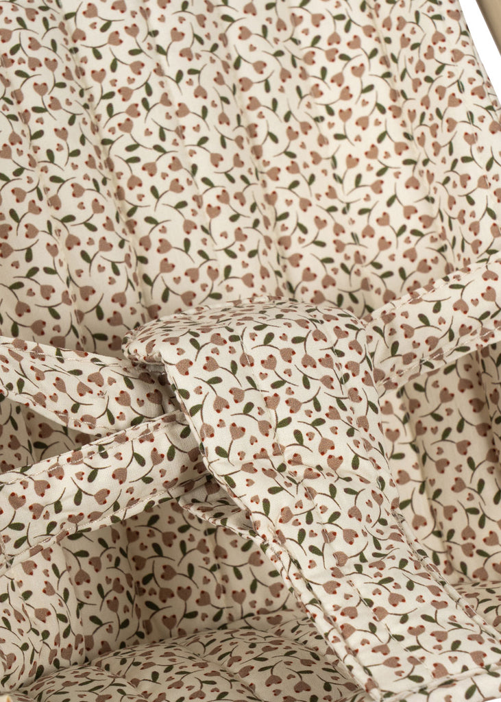 A close-up of the Konges Sloejd Doll Stroller - Milk Tank shows a padded fabric seat with a small pink and green floral print, featuring harness straps designed for secure seating.