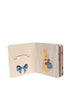 The Konges Sloejd Touch and Feel Book features a blue bow illustration on the left page and a rabbit in a blue jacket on the right, set against striped and floral backgrounds.