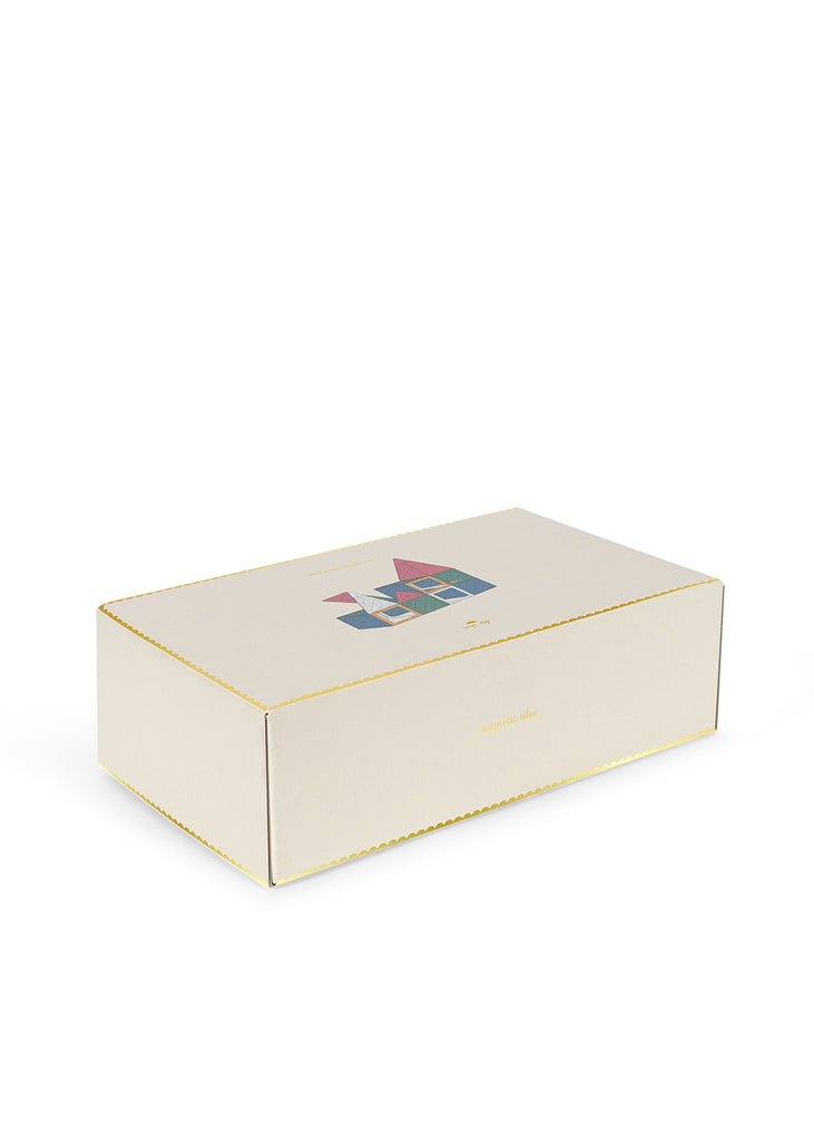 A Konges Sloejd Piece By Piece Magentic Building Set in a rectangular box with a scalloped gold border, featuring a small illustration of a house made from magnetic tiles and the text “magnetic tiles” on the lid.
