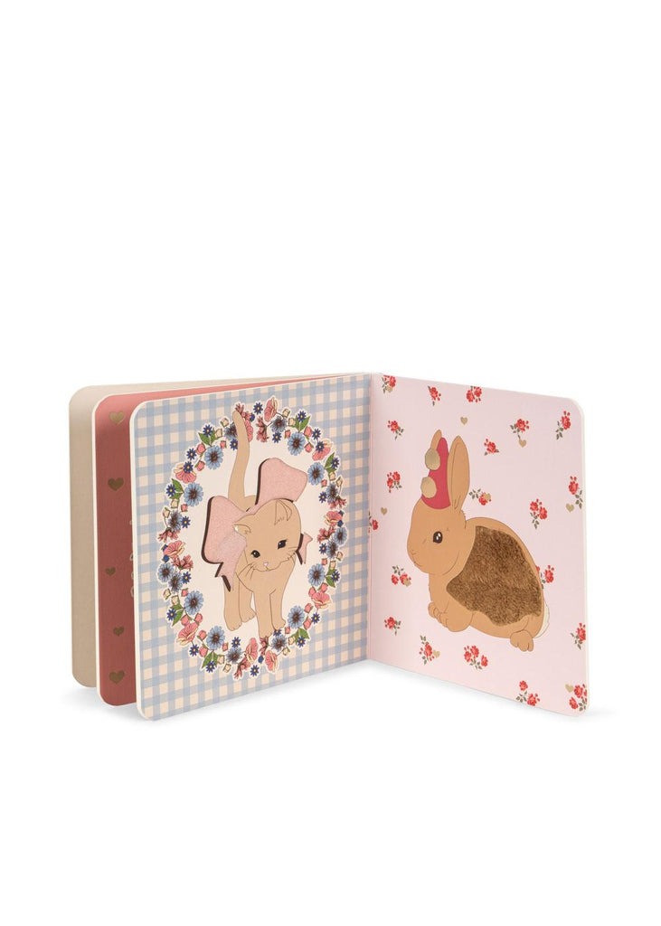 The Konges Sloejd Touch and Feel Book features a kitten with a pink bow on the left page and a brown bunny with a party hat on the right, both surrounded by flowers and playful designs.