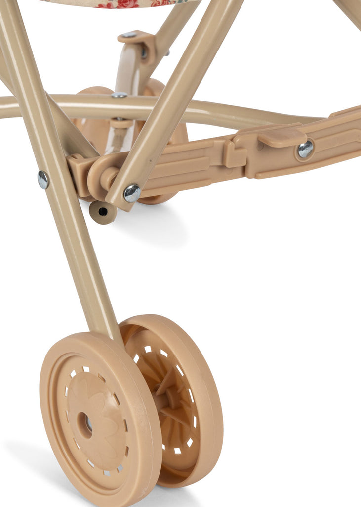 Close-up of the lower part of the Konges Sloejd Doll Stroller - Lumina, highlighting the beige double wheels and sturdy metal frame with screws connecting each part.
