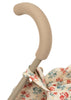 Close-up of the Konges Sloejd Doll Stroller - Lumina handle with a tan padded grip. The stroller has cream fabric with a red and blue floral print and sturdy double wheels.