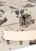 Close-up of the Konges Sloejd Music Set - Circus: a whimsical musical suitcase featuring a metal latch, cream fabric handle, and playful circus-themed illustrations of people, stars, and ships on a beige background—a charming accessory for carrying your favorite wooden instruments or complete music set.