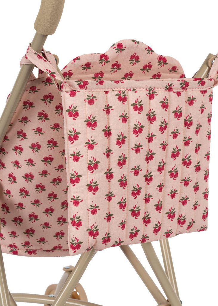 A close-up of a pink quilted bag with a red floral print, hanging from the handle of the Konges Sloejd Doll Stroller - Rosie Rose—a charming and practical addition to your doll accessories collection.