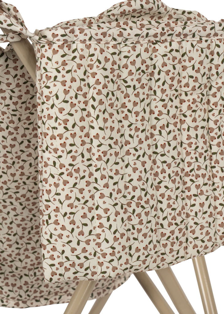 A close-up of the Konges Sloejd Doll Stroller - Milk Tank, featuring a cream fabric with a small brown and green floral pattern, draped over its light wooden legs and double wheels.