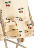 A close-up of the Konges Sloejd Twin Doll Stroller - Cherry shows its padded cream-colored seats with red cherry and green leaf patterns, safety straps, and a light beige metal frame.
