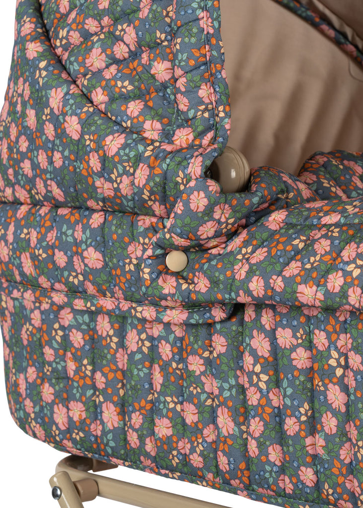 Close-up of the Konges Sloejd Doll Pram - Kyoto, featuring quilted fabric with pink, orange, and green floral patterns on a blue background; partially visible beige metal frame adds to its vintage look.