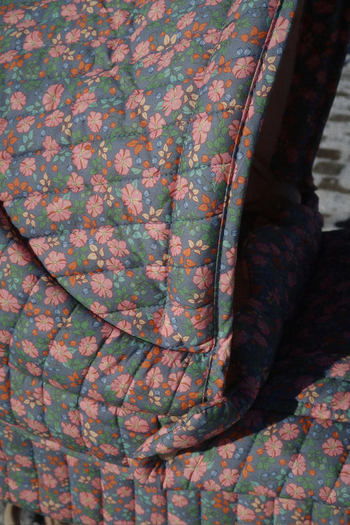 A close-up of the Konges Sloejd Doll Pram - Kyoto’s quilted fabric, featuring a pink and orange floral pattern on a blue background, with sunlight casting gentle shadows.