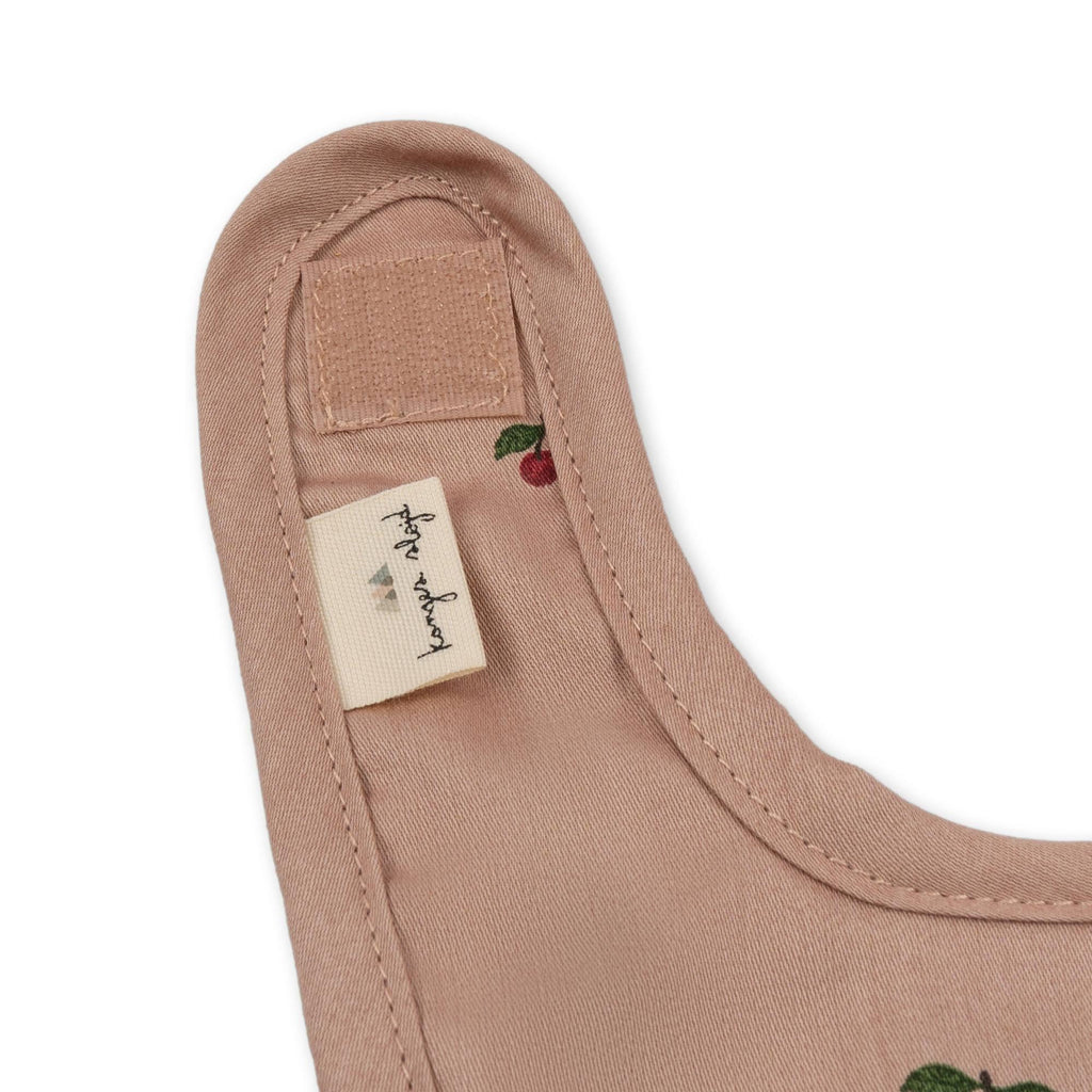 Close-up of the Konges Sloejd Doll Nursery Set - Cherry Blush shows pink organic cotton fabric with small cherry prints, a velcro fastener, and a sewn-in "konges sloejd" label.