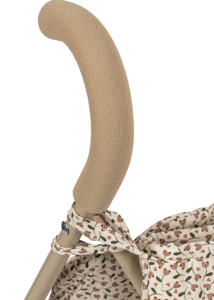 Close-up of the Konges Sloejd Doll Stroller - Milk Tank handle, covered in beige foam and wrapped with fabric featuring a delicate brown and green leaf pattern.