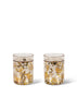 The Konges Sloejd Glitter Cup - Let's Go Bananas features gold and yellow banana and confetti designs, filled with a light-colored drink—an eye-catching choice for playful kids' dinnerware.