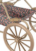 Close-up of the Konges Sloejd Doll Pram - Kyoto, featuring large beige wheels and a floral seat with pink and orange flowers on a dark background, plus a padded mattress for added comfort.