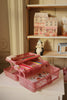 A Konges Sloejd Creative Art Caddy in Glitter Rose sits open on a small table, filled with colored pencils and stickers. Behind it, shelves display a panda figurine, paper house models, and a ceramic cat.