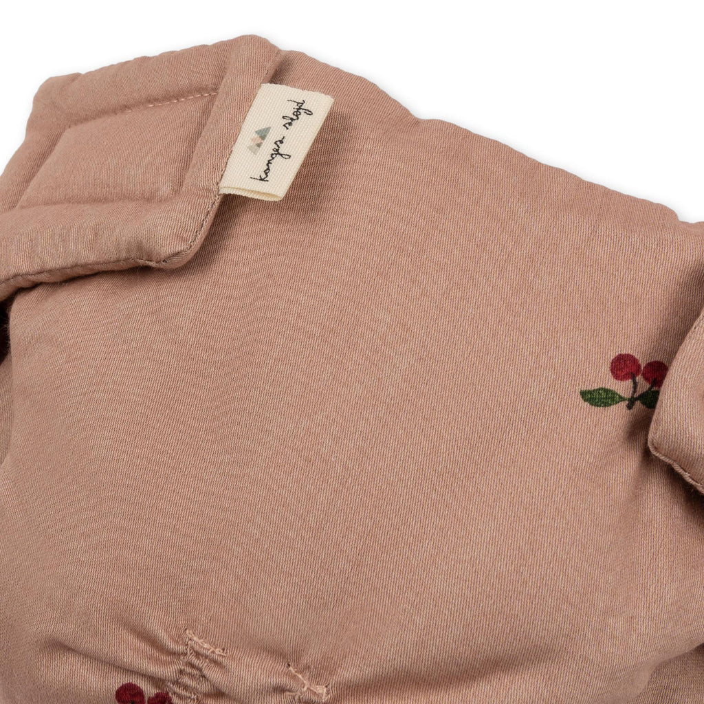 Close-up of the Konges Sloejd Doll Nursery Set in Cherry Blush—soft dusty pink organic cotton with red berry and green leaf embroidery, finished with a beige “konges slojd” tag.