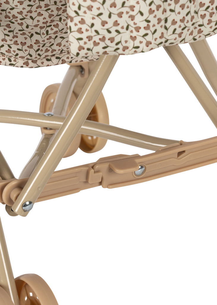 Close-up of the Konges Sloejd Doll Stroller - Milk Tank, featuring a beige frame with floral fabric, double wheels, support bars, and a locking mechanism.