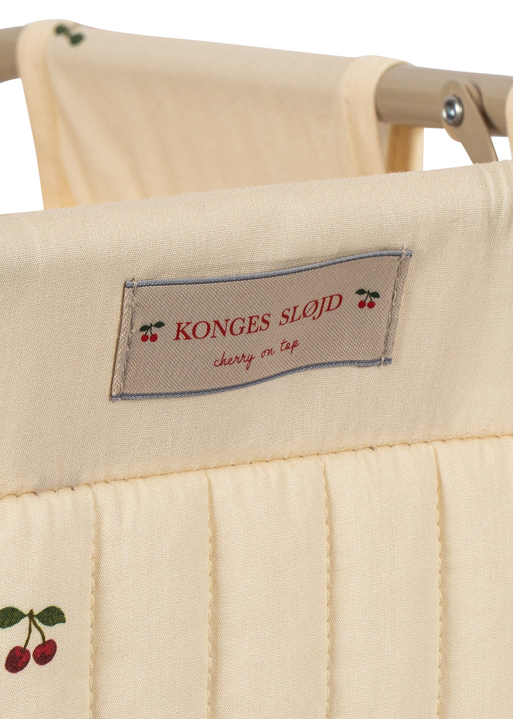 Close-up of the cream-colored quilted fabric on the Konges Sloejd Stoller Kids Wagon - Cherry, featuring embroidered cherries and a “Konges Sløjd, cherry on top” label, attached to a wooden frame.