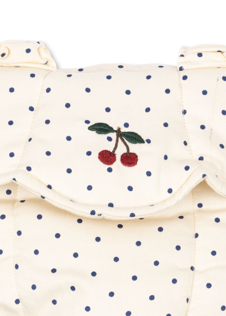 The Konges Sloejd Doll Carrier - Estate Dot is a cream-colored cotton carrier with small navy blue polka dots and a flap embroidered with red cherries and green leaves, perfect for carrying dolls in style.