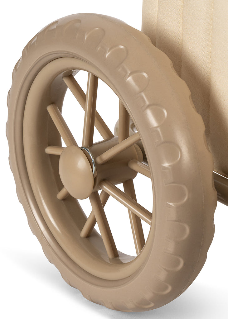 Close-up of a beige plastic wheel with a textured tread and multiple spokes, attached to the light-colored frame of the Konges Sloejd Stroller Kids Wagon - Cherry, typical of a children’s stroller or toy wagon.