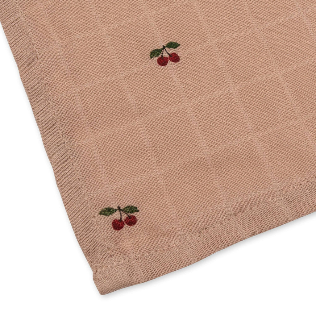 A close-up of the Konges Sloejd Doll Nursery Set - Cherry Blush shows a light brown checkered fabric napkin with embroidered red cherries and green leaves in the corners, made for doll accessories.