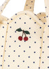 Close-up of the cream-colored Konges Sloejd Doll Lift - Estate Dot, featuring OEKO-TEX certified fabric with navy polka dots and red embroidered cherries; part of a padded cotton doll carrier.