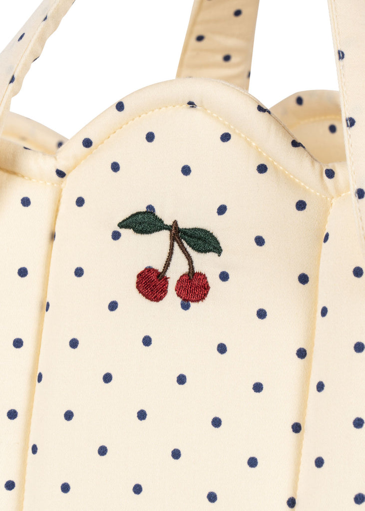 Close-up of the cream-colored Konges Sloejd Doll Lift - Estate Dot, featuring OEKO-TEX certified fabric with navy polka dots and red embroidered cherries; part of a padded cotton doll carrier.