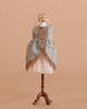 The Maileg Princess Dress for Big Sister Mouse features blue-gray fabric, gold lace trim, and a peach underskirt on a small wooden dress form with a gold crown, all set against a solid beige background.