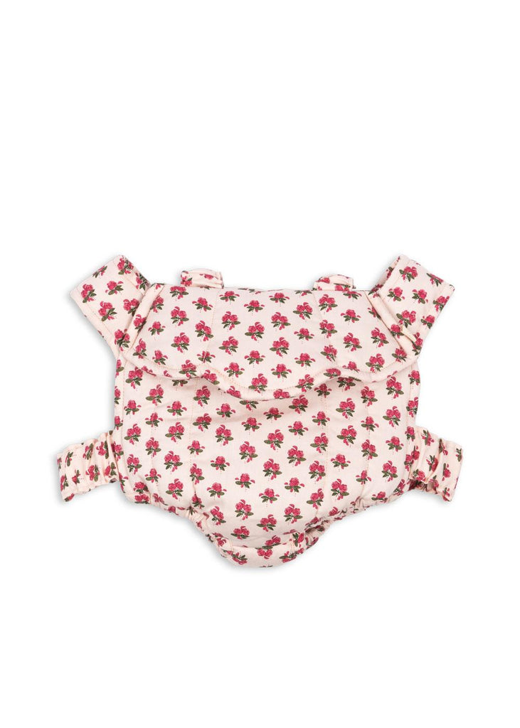 The Konges Sloejd Doll Carrier - Rosie Rose features soft pink cotton with red floral patterns, adjustable shoulder straps, and a waist strap, shown on a plain white background.