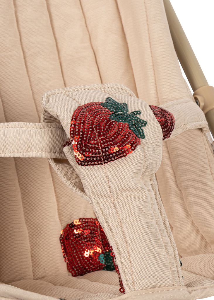 Close-up of the Konges Sloejd Doll Stroller - Strawberry, featuring a beige padded harness with red sequined strawberry appliqués, green leaves, and vertical quilting—a soft, stylish addition to any doll stroller or carriage bag with double wheels.