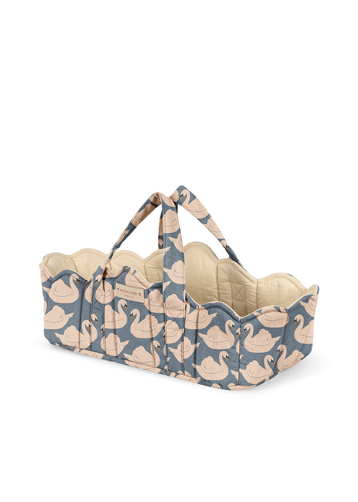 Introducing the Konges Sloejd Doll Lift - Swan: a beautifully quilted doll carrier basket featuring scalloped edges, dual handles, and a charming blue fabric adorned with white swan motifs. The interior is lined with soft cream-colored material for added comfort. Made from OEKO-TEX certified cotton, this padded doll lift provides a cozy and safe way for your little one to carry their favorite toy.