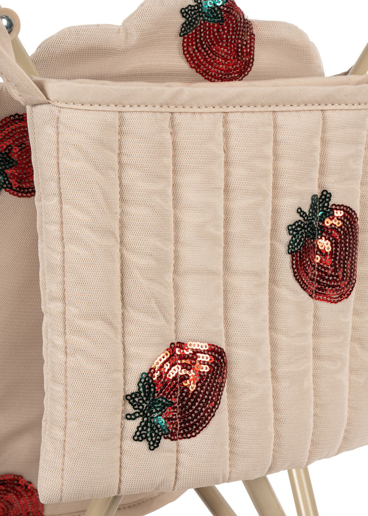 A close-up of the Konges Sloejd Doll Stroller - Strawberry, featuring a beige quilted bag with sequined red strawberries and green leaves. The removable fabric adds versatility, and its playful look is perfect for stylish doll outings.