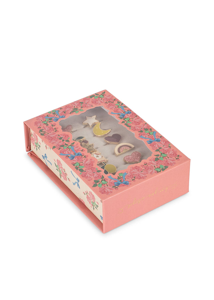A pink floral box adorned with decorative motifs and a clear window displays the Konges Sloejd 12 Pack Ring Set. The closed box, featuring assorted pastel-colored rings shaped like stars, hearts, and moons, rests on a white surface.