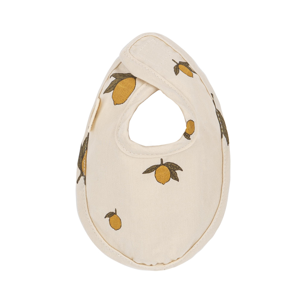 The Konges Sloejd Doll Nursery Set - Lemon features a cream-colored bib with Velcro closure, adorned with yellow lemons and green leaves—an ideal accessory for any organic cotton doll collection.