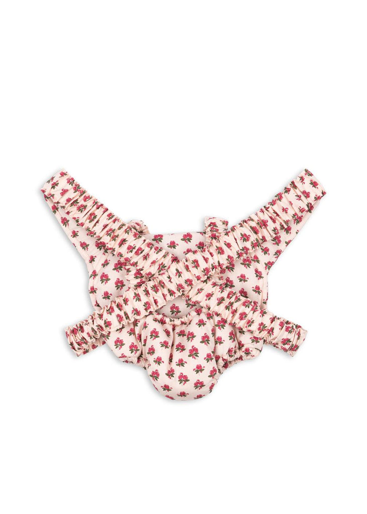The Konges Sloejd Doll Carrier - Rosie Rose features a white background with a pink floral print and ruffled, adjustable straps—an adorable toy accessory to complement any cotton doll carrier.