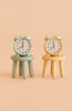 Two small alarm clocks, one blue and one yellow, are displayed atop the Maileg Stool Set, Mouse - Mint/Light Yellow, their beech wood construction and vintage paint finish adding charm against a beige background.